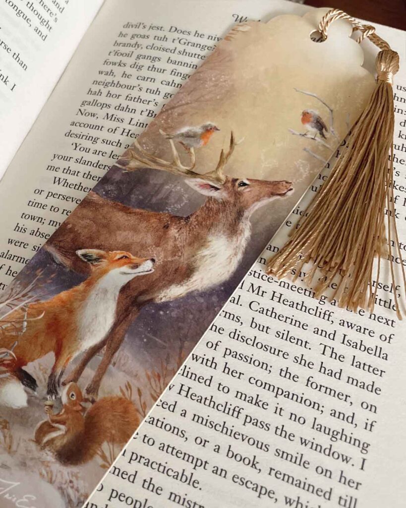 Illustrated winter bookmark featuring a deer, fox, robin, squirrel, and snowy woodland scene with a gold tassel.
