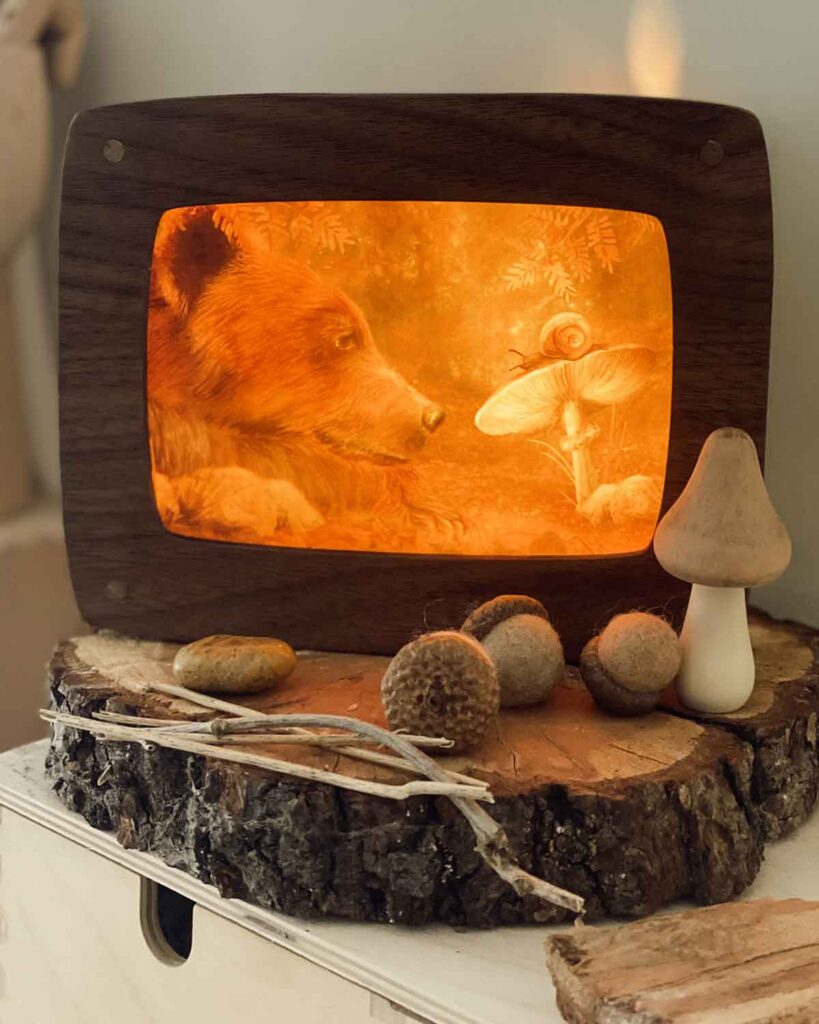 Illuminated wooden shadow box displaying bear and snail scene with acorns and ceramic mushroom on wood slice base