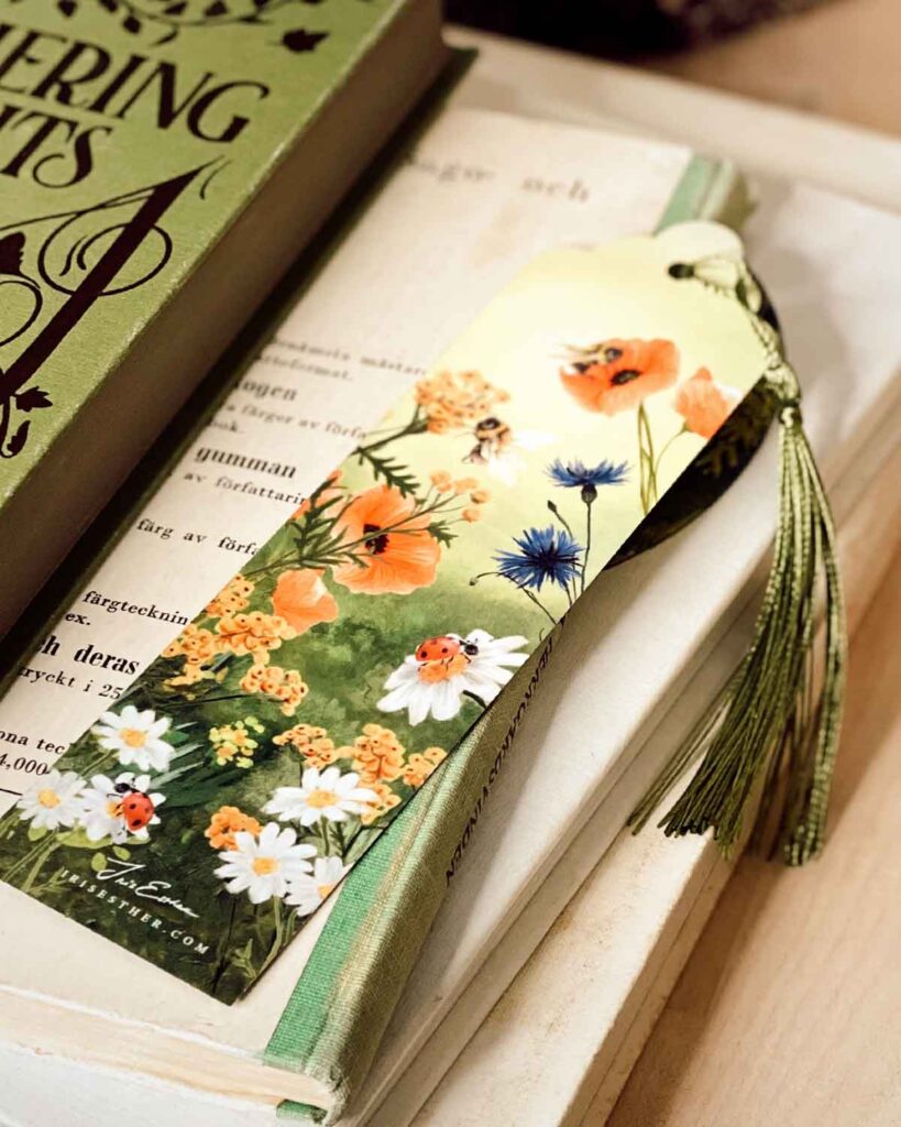 Illustrated bookmark with bees, ladybugs, and summer wildflowers like poppies, daisies, and cornflowers, finished with a green tassel.