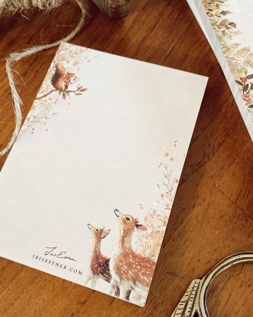 blush colored mini notepad with leaves fluttering and two deers and a squirrel holding berries