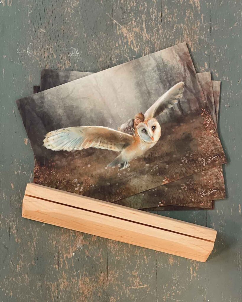 Watercolor prints of barn owl in flight stacked on weathered green wood surface with wooden frame piece