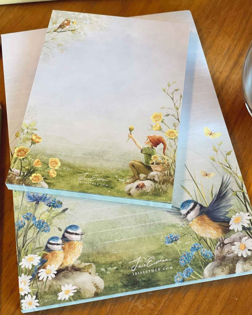 Decorative stationery paper featuring watercolor illustrations of birds, flowers, and garden scenes on wooden table